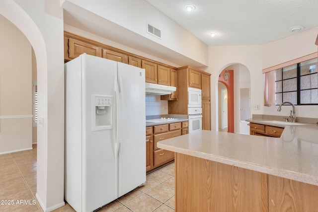 kitchen with under cabinet range hood, white appliances, visible vents, light countertops, and tasteful backsplash