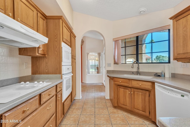 kitchen featuring white appliances, backsplash, a sink, and under cabinet range hood