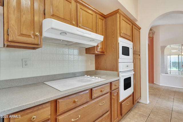 kitchen with white appliances, tasteful backsplash, light countertops, under cabinet range hood, and light tile patterned flooring