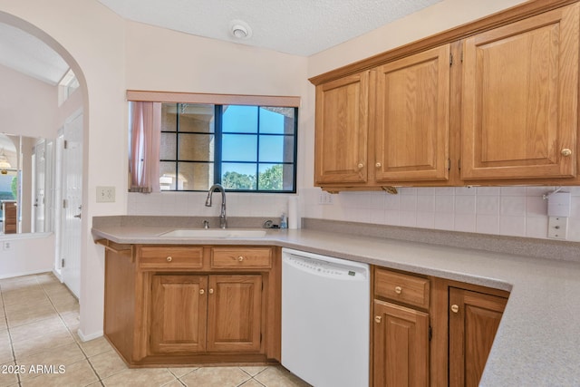 kitchen featuring arched walkways, light countertops, decorative backsplash, a sink, and dishwasher