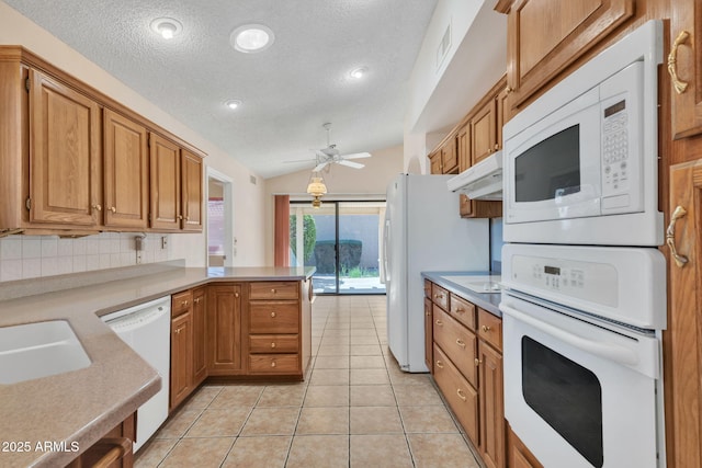 kitchen featuring light tile patterned floors, light countertops, vaulted ceiling, white appliances, and a peninsula