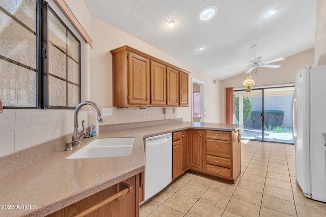 kitchen with light countertops, vaulted ceiling, a sink, white appliances, and a peninsula