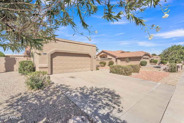 pueblo revival-style home with a garage, fence, concrete driveway, and stucco siding