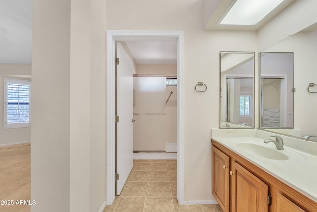 full bathroom featuring a skylight, baseboards, tile patterned floors, walk in shower, and vanity