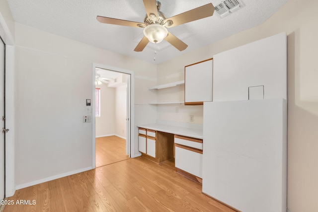 interior space with visible vents, light wood-style floors, built in study area, a textured ceiling, and baseboards