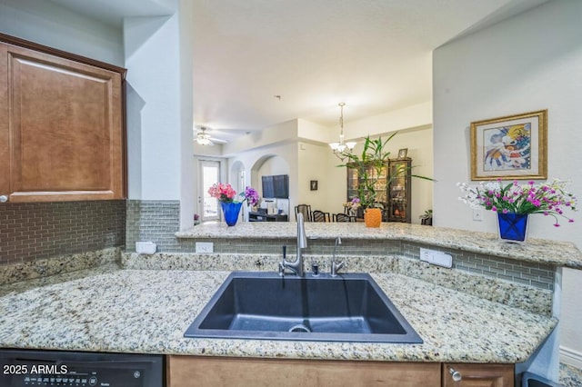 kitchen with a sink, dishwashing machine, decorative backsplash, and light stone countertops