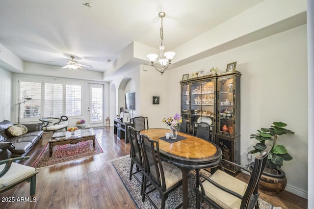 dining room featuring arched walkways, ceiling fan with notable chandelier, and wood finished floors