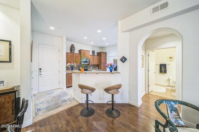 kitchen featuring stainless steel microwave, visible vents, brown cabinetry, and wood finished floors