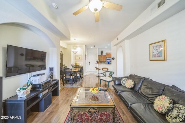 living room featuring arched walkways, visible vents, wood finished floors, and ceiling fan with notable chandelier
