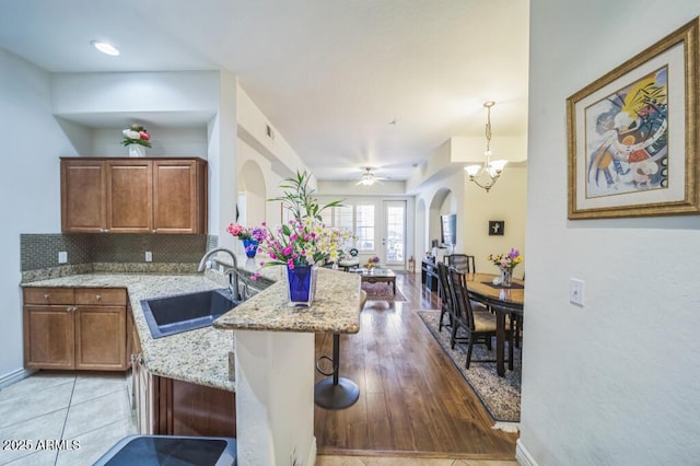kitchen with light stone countertops, a sink, arched walkways, a peninsula, and tasteful backsplash