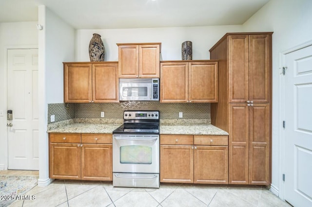 kitchen featuring appliances with stainless steel finishes, brown cabinetry, backsplash, and light stone counters