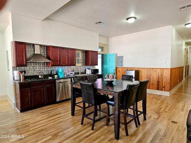 interior space featuring black gas stovetop, wall chimney exhaust hood, dishwasher, light hardwood / wood-style flooring, and electric panel
