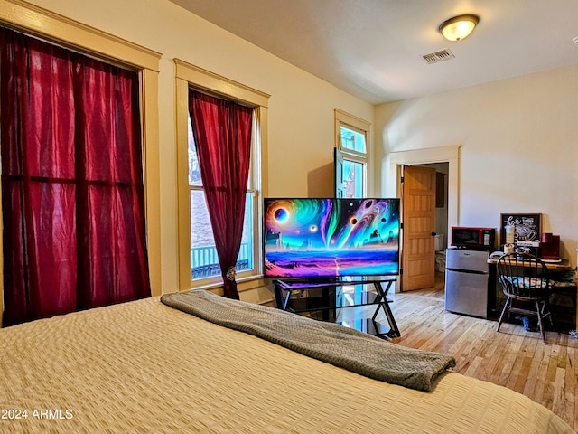 bedroom with stainless steel fridge and light wood-type flooring
