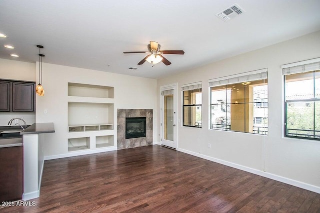 20750 N 87th St Unit 2103, Scottsdale, AZ 85255 - unfurnished living room featuring built in shelves, a ceiling fan, baseboards, dark wood-style flooring, and a tiled fireplace