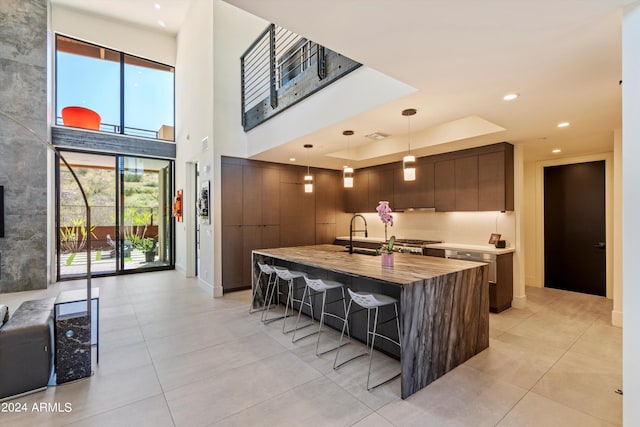 kitchen with dark brown cabinets, a breakfast bar, a tray ceiling, a kitchen island with sink, and hanging light fixtures