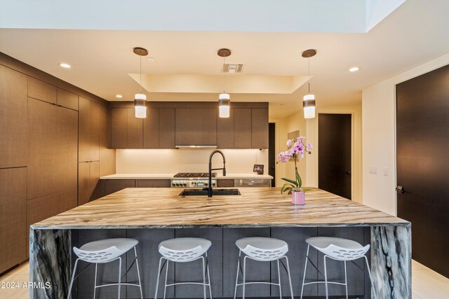 kitchen with a center island with sink, sink, light tile patterned floors, and decorative light fixtures