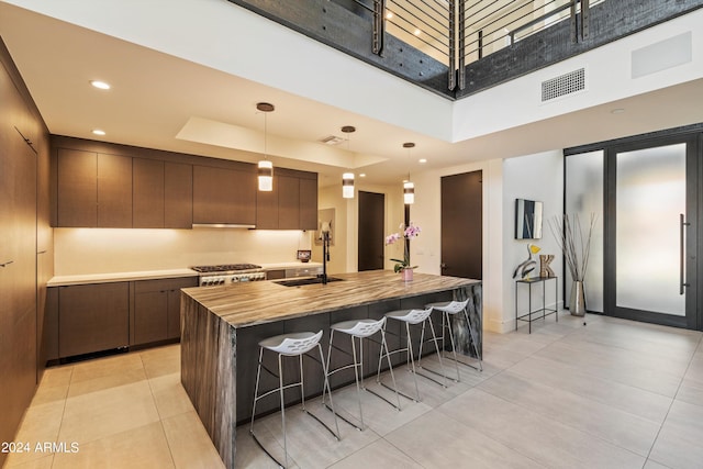 kitchen with hanging light fixtures, a center island with sink, sink, and stainless steel range