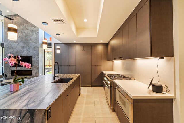 kitchen featuring light tile patterned flooring, hanging light fixtures, sink, high end stainless steel range oven, and a fireplace