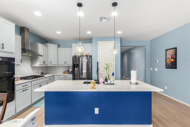 kitchen with decorative backsplash, appliances with stainless steel finishes, a kitchen island with sink, and wall chimney exhaust hood