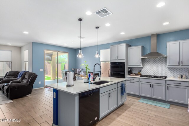 kitchen featuring tasteful backsplash, wall chimney range hood, black appliances, pendant lighting, and sink