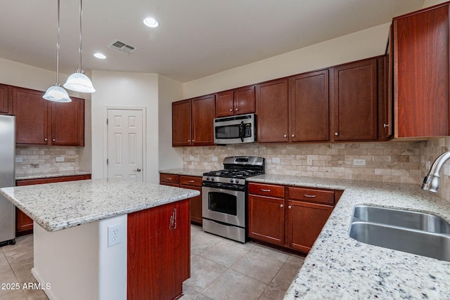 kitchen featuring sink, stainless steel appliances, light stone counters, a kitchen island, and decorative light fixtures