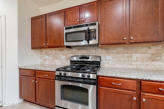 kitchen with appliances with stainless steel finishes, light stone counters, and decorative backsplash