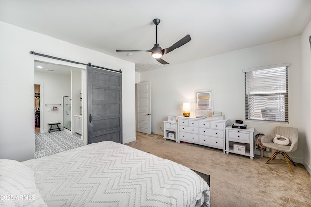 bedroom with a walk in closet, baseboards, a barn door, light carpet, and a ceiling fan