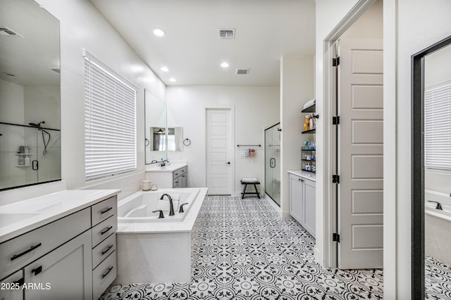 bathroom featuring visible vents, two vanities, a stall shower, recessed lighting, and a bath