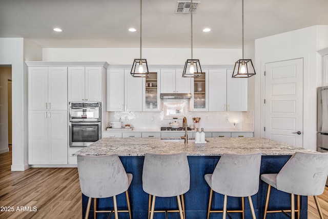 kitchen featuring visible vents, stainless steel double oven, a sink, under cabinet range hood, and light wood-type flooring