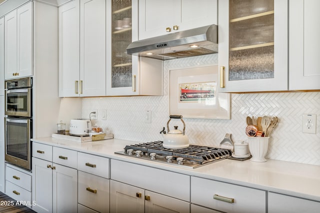 kitchen with under cabinet range hood, white cabinetry, appliances with stainless steel finishes, light countertops, and decorative backsplash