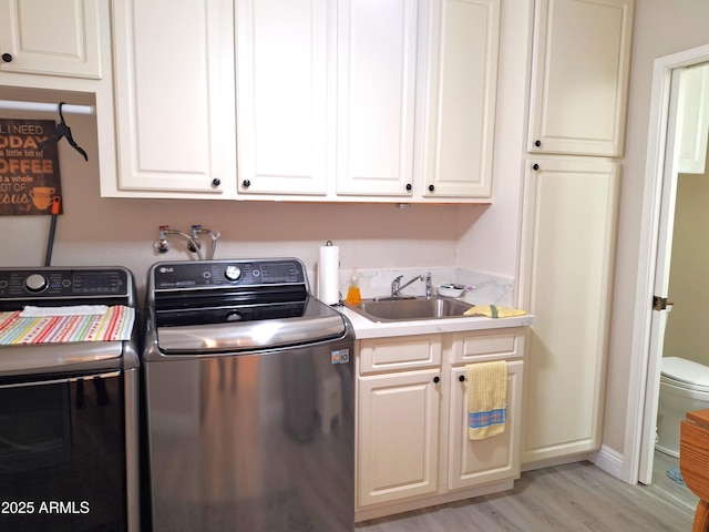 clothes washing area with washing machine and clothes dryer, sink, cabinets, and light hardwood / wood-style flooring