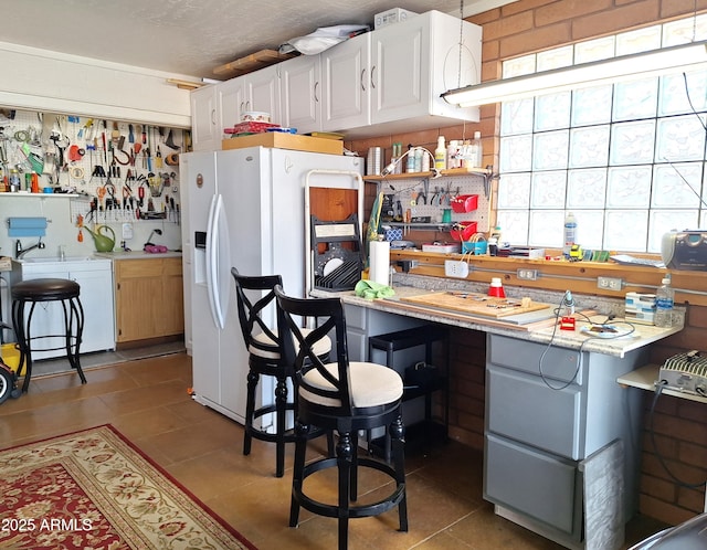 kitchen with white refrigerator with ice dispenser, light tile patterned floors, and white cabinetry