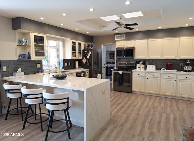 kitchen featuring kitchen peninsula, appliances with stainless steel finishes, a skylight, a raised ceiling, and white cabinets