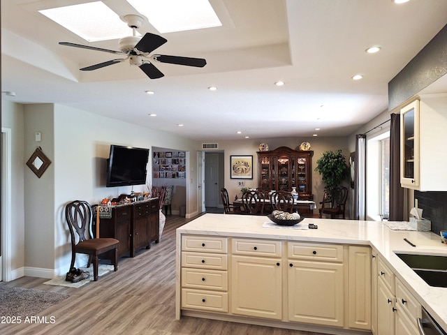 kitchen with light hardwood / wood-style flooring, stainless steel dishwasher, ceiling fan, cream cabinetry, and light stone counters