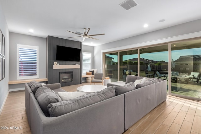 living room featuring a large fireplace, ceiling fan, and light wood-type flooring