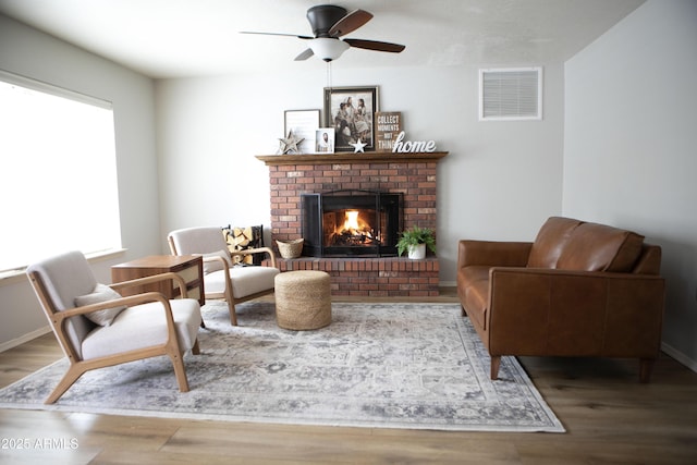 living area featuring a brick fireplace, ceiling fan, and wood-type flooring