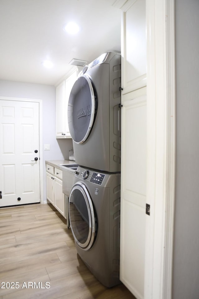 laundry area with stacked washing maching and dryer, light hardwood / wood-style floors, and cabinets