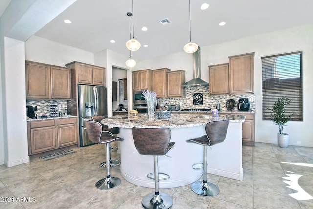 kitchen with light stone countertops, wall chimney exhaust hood, a kitchen breakfast bar, an island with sink, and appliances with stainless steel finishes