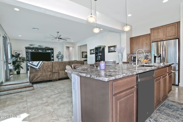 kitchen with stainless steel refrigerator with ice dispenser, light stone counters, a kitchen island with sink, decorative light fixtures, and black dishwasher