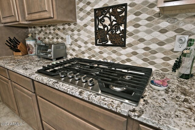 kitchen with stainless steel gas stovetop, light tile patterned flooring, light stone counters, and backsplash