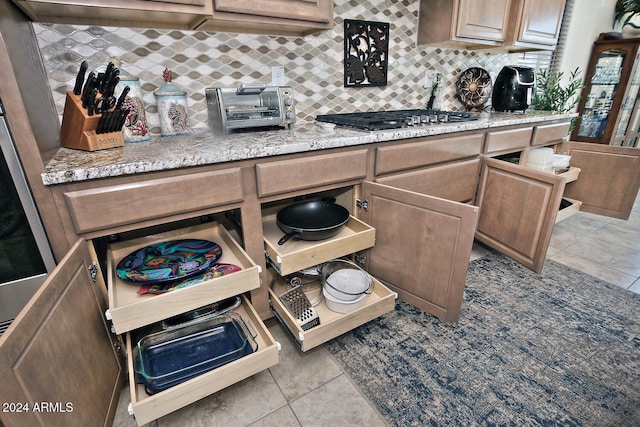 kitchen featuring light stone countertops, light tile patterned floors, decorative backsplash, and stainless steel gas cooktop