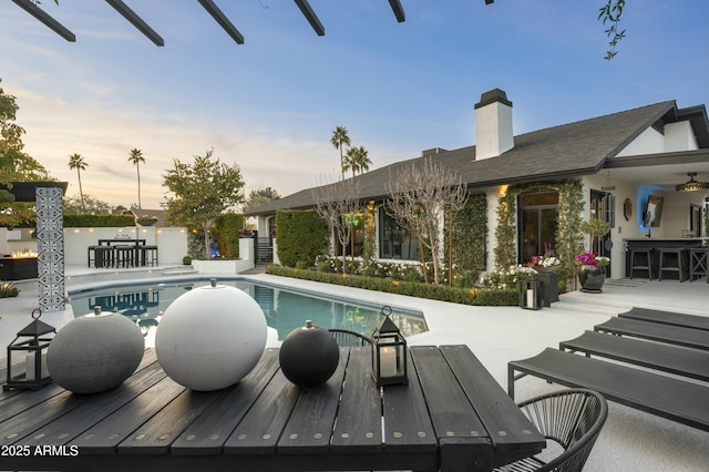 pool at dusk featuring a patio area and an outdoor bar