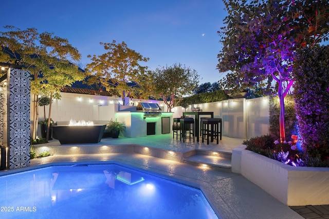 pool at dusk featuring exterior kitchen, a patio, area for grilling, and a fire pit