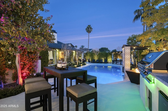 pool at dusk featuring a patio and an outdoor kitchen