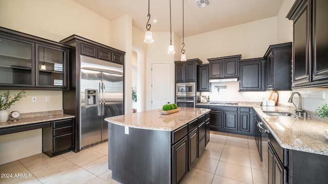 kitchen with light tile patterned flooring, sink, built in appliances, decorative light fixtures, and a kitchen island