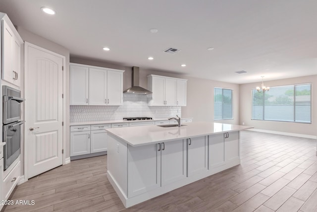 kitchen with white cabinetry, sink, wall chimney exhaust hood, and an island with sink