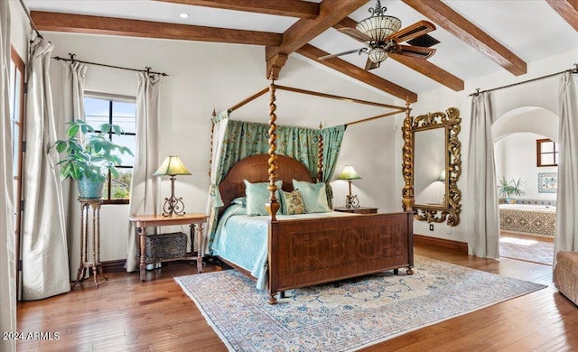 bedroom with connected bathroom, ceiling fan, wood-type flooring, and vaulted ceiling with beams