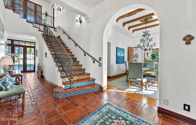 entrance foyer featuring a high ceiling, french doors, dark tile patterned flooring, beamed ceiling, and a notable chandelier