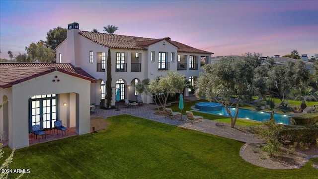 back house at dusk featuring french doors, a patio area, and a lawn