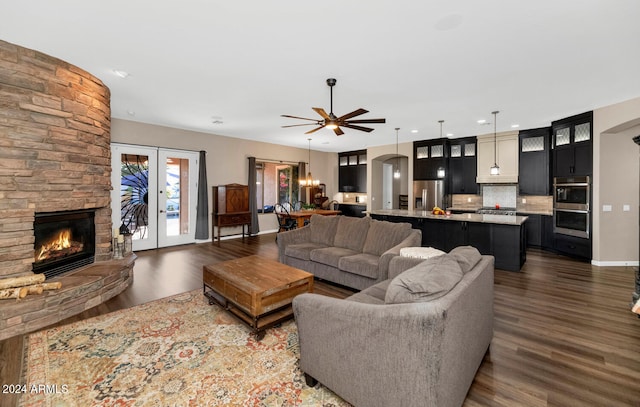 living room with french doors, dark hardwood / wood-style flooring, a stone fireplace, and ceiling fan